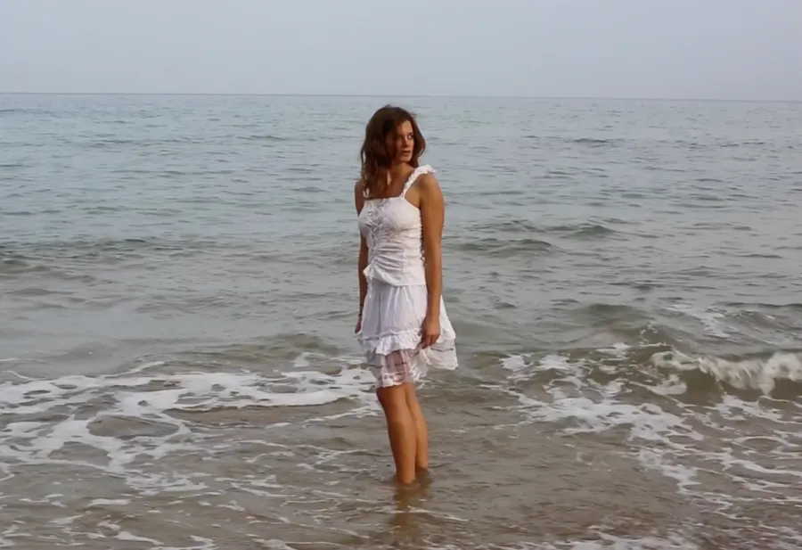 A woman in a white dress stands in the shallow sea