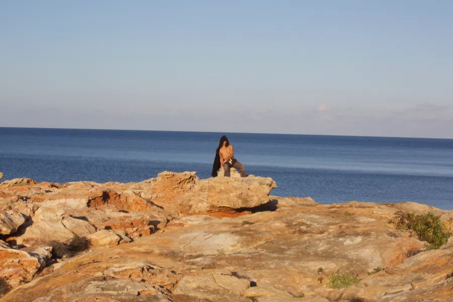 A woman sits alone on sunlit rocks by the sea