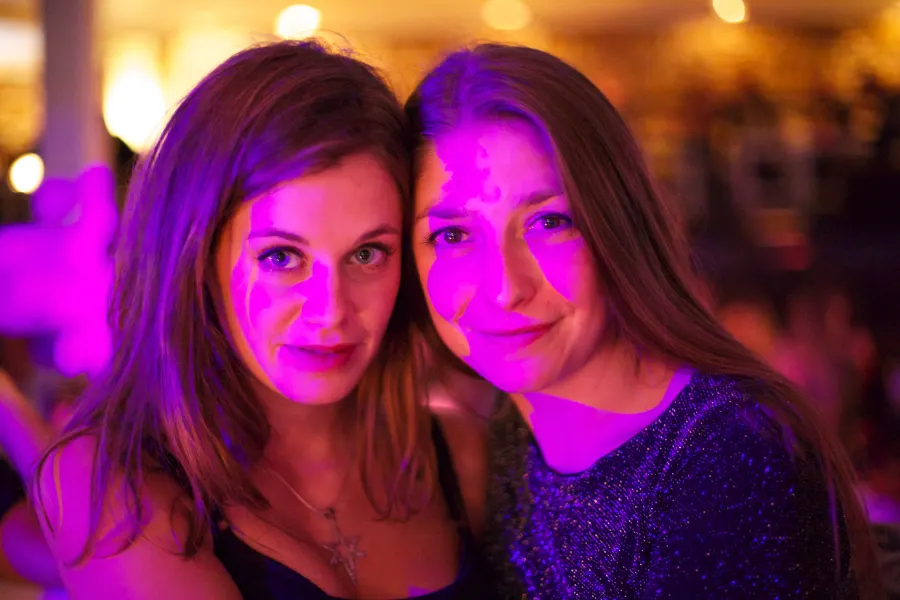 Two women smile into the camera in pink club light