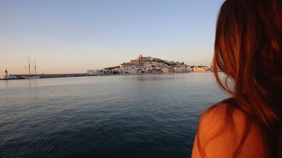 Evening view across the harbour to Ibiza old town, a woman in the foreground