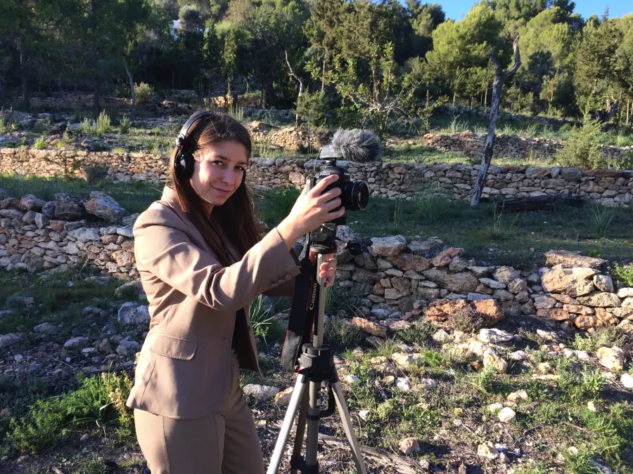 A woman films with a camera in a dry island landscape